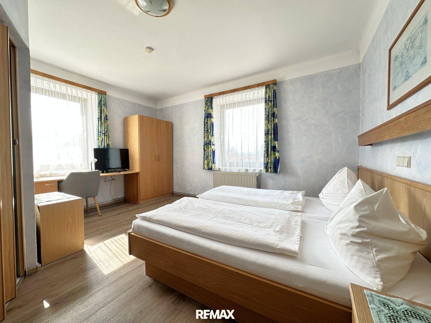Helles Schlafzimmer mit Doppelbett, Schreibtisch, Kleiderschrank und Laminatboden.