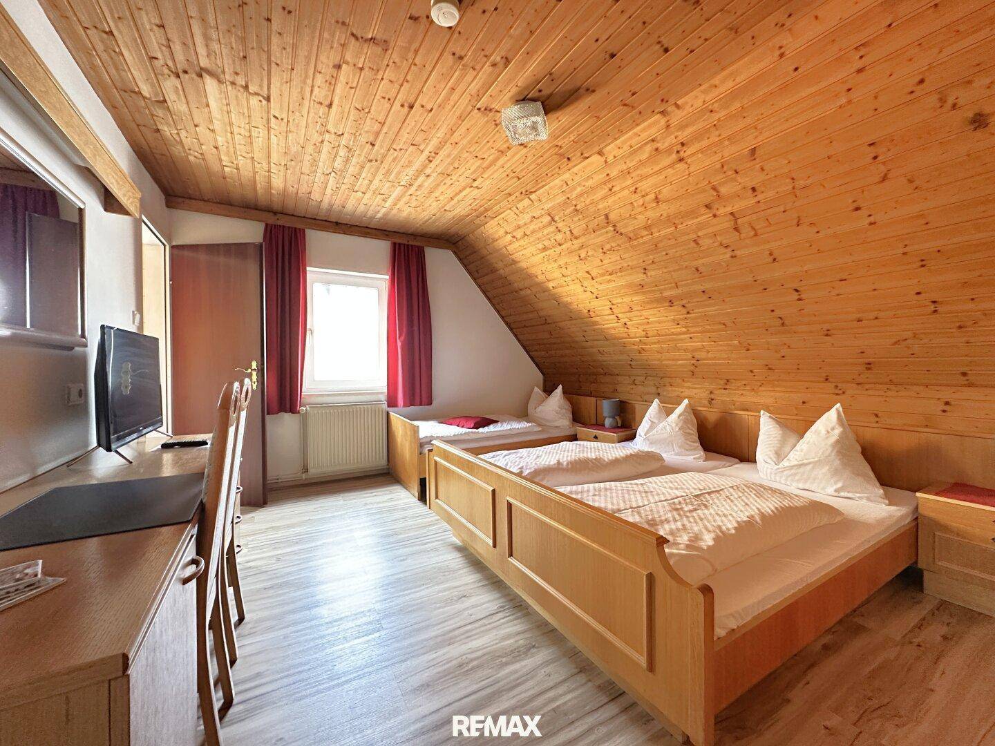 Gemütliches Schlafzimmer mit zwei Betten, Schreibtisch und einer markanten Holzdecke mit Dachschräge.