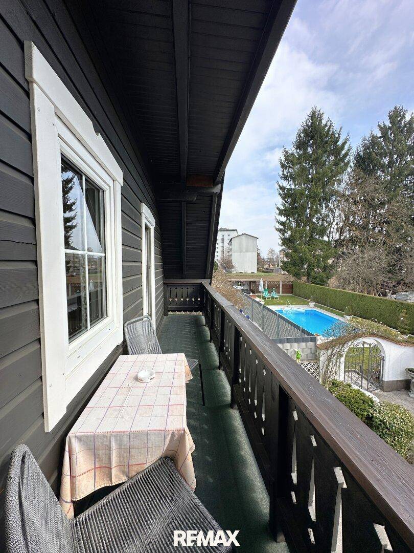 Balkon mit Sitzgelegenheiten und Blick auf einen Garten mit Swimmingpool und Bäumen.