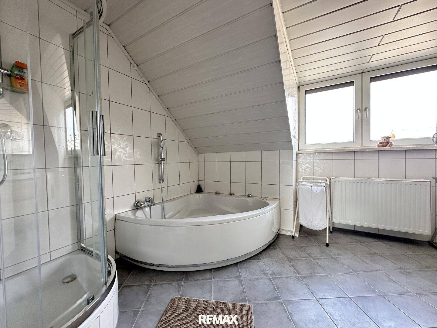 Geräumiges Badezimmer mit Duschkabine, Eckbadewanne, Dachschräge und Fenster.