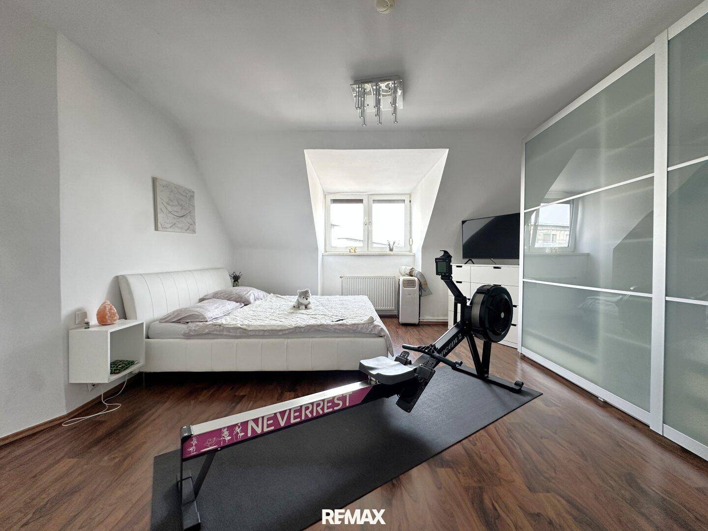 Schlafzimmer mit Doppelbett, Dachschräge, Schiebetürenschrank und Rudergerät.