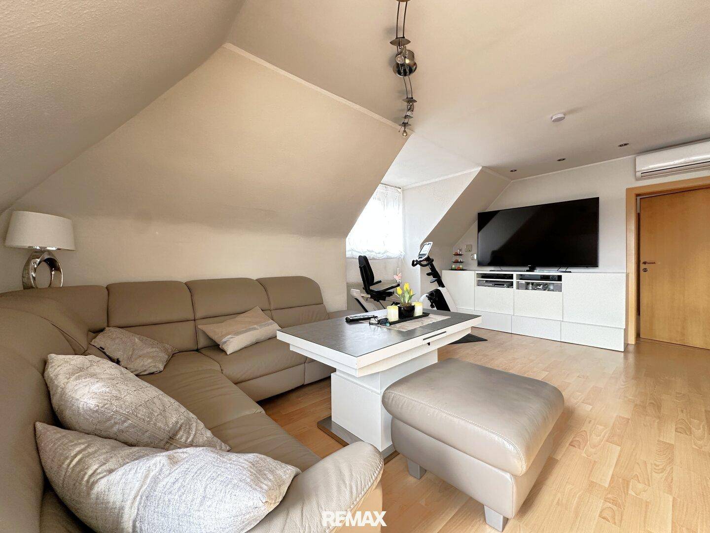Gemütliches Wohnzimmer mit großem Ecksofa, Couchtisch und Fernseher unter einer Dachschräge.