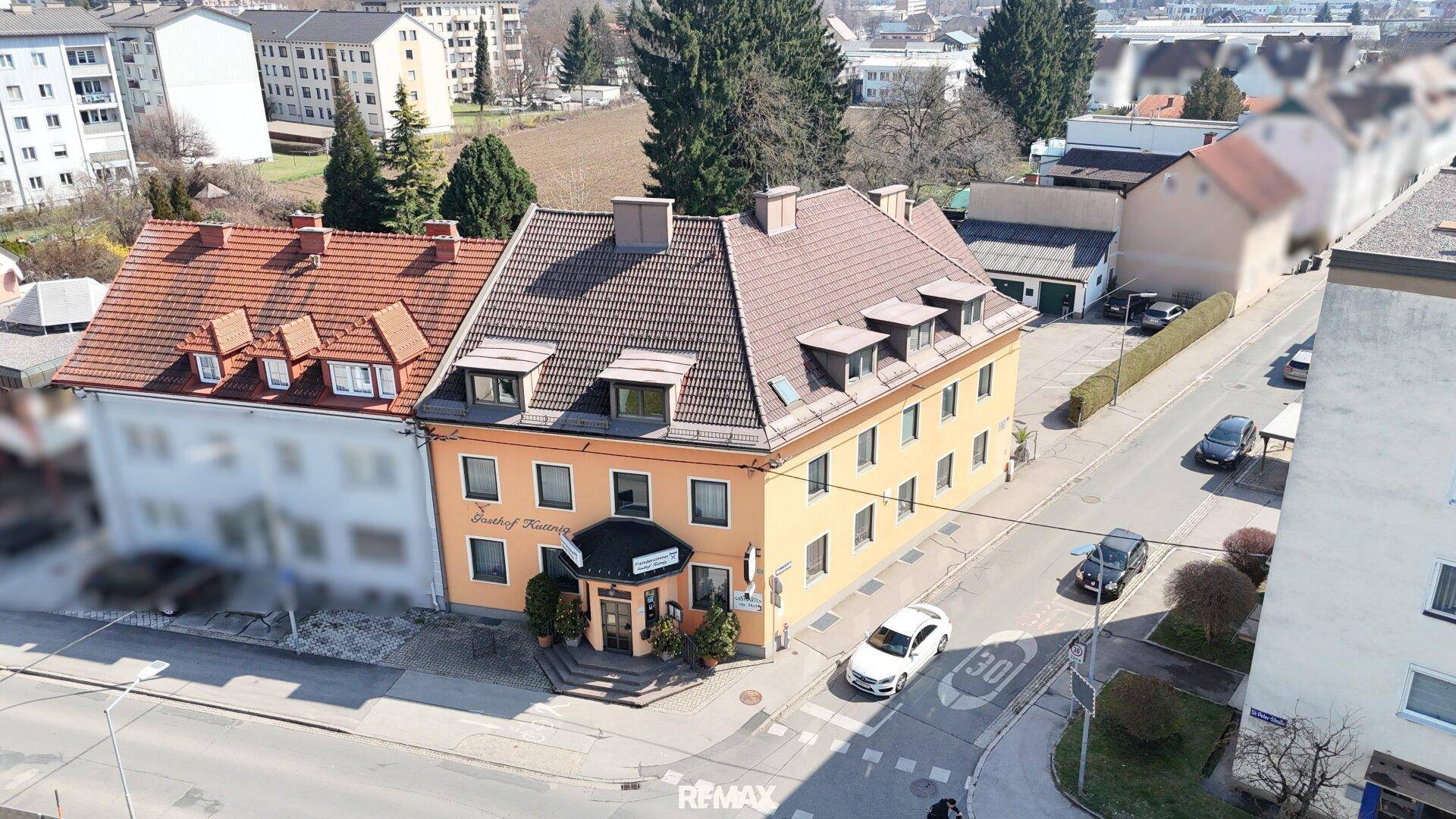 Luftaufnahme eines Gasthofs mit umliegenden Gebäuden und einer Straße in einer städtischen Umgebung.