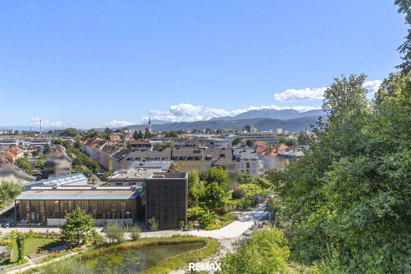 Weitläufiger Blick über eine Stadtlandschaft mit viel Grün und Bergen im Hintergrund.