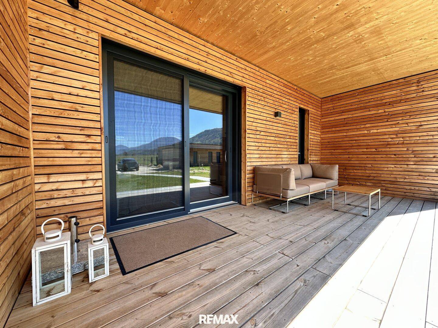 Überdachte Holzterrasse mit Schiebetür und gemütlicher Sitzgelegenheit im Freien.