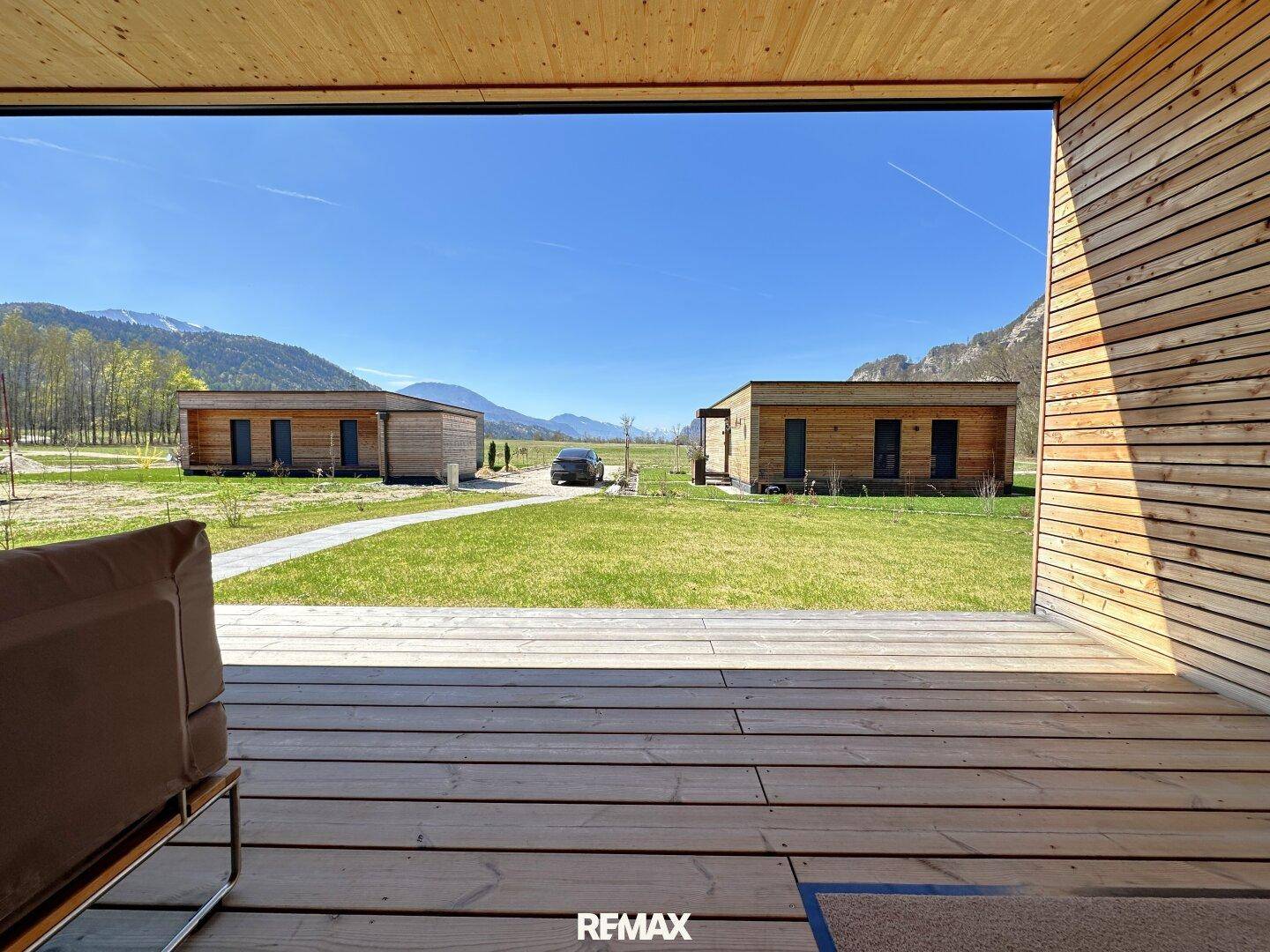 Blick von der überdachten Terrasse auf weitere moderne Holzhäuser und die umliegende Berglandschaft.