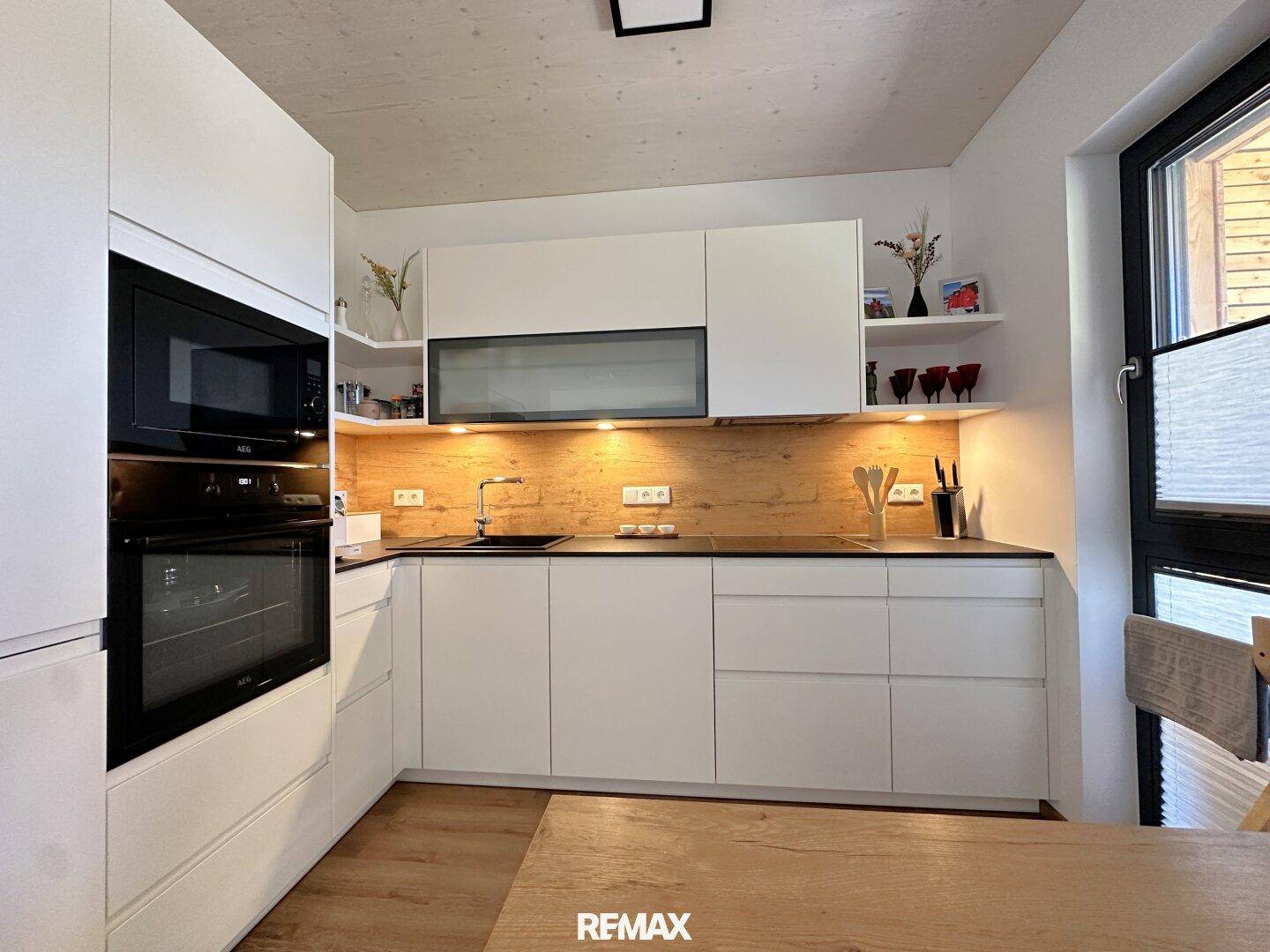 Moderne Einbauküche mit weißen Fronten, Holzrückwand und integrierten Elektrogeräten.