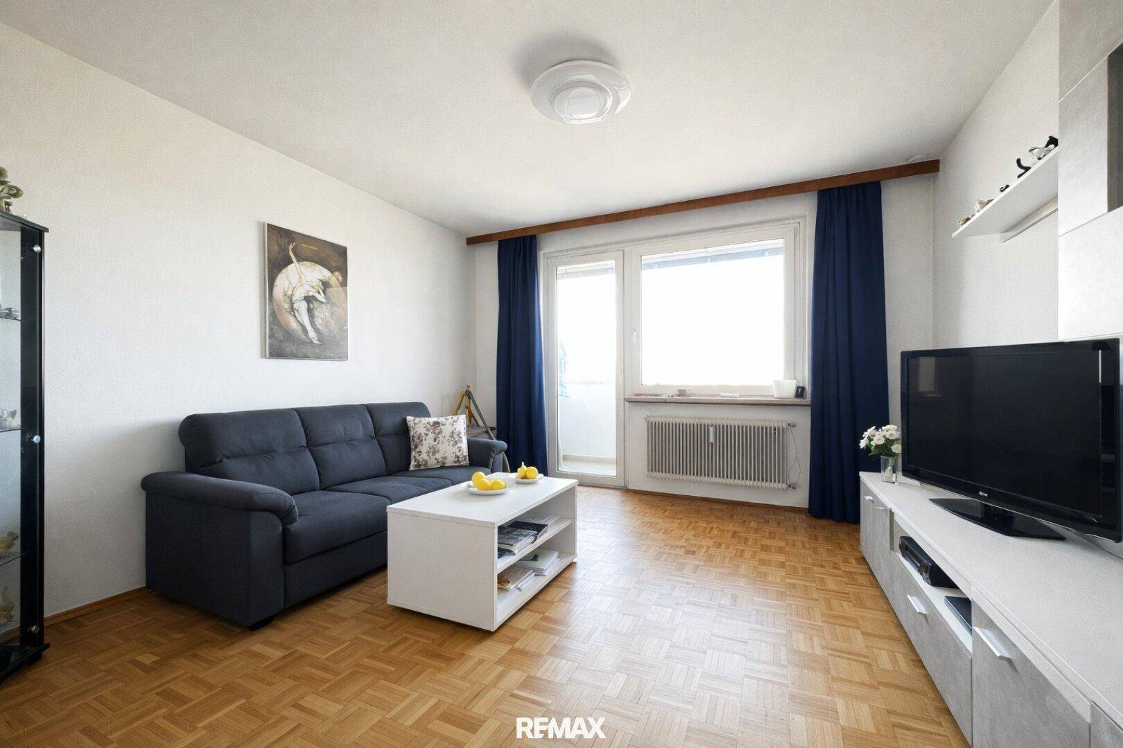 Gemütliches Wohnzimmer mit Parkettboden, Sofa und Zugang zum Balkon.