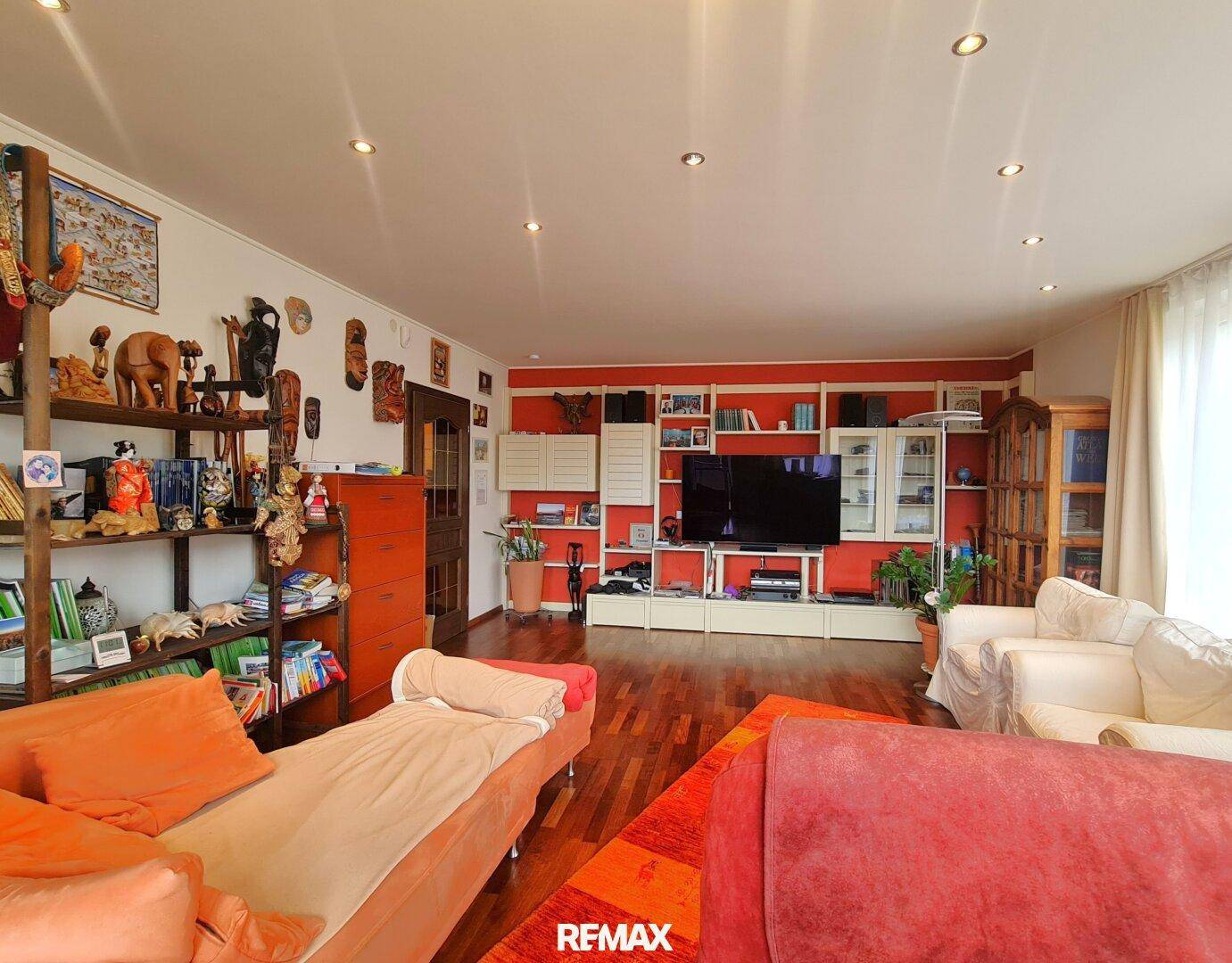 Wohnzimmer mit Parkettboden, roter Akzentwand und vielfältiger Dekoration.