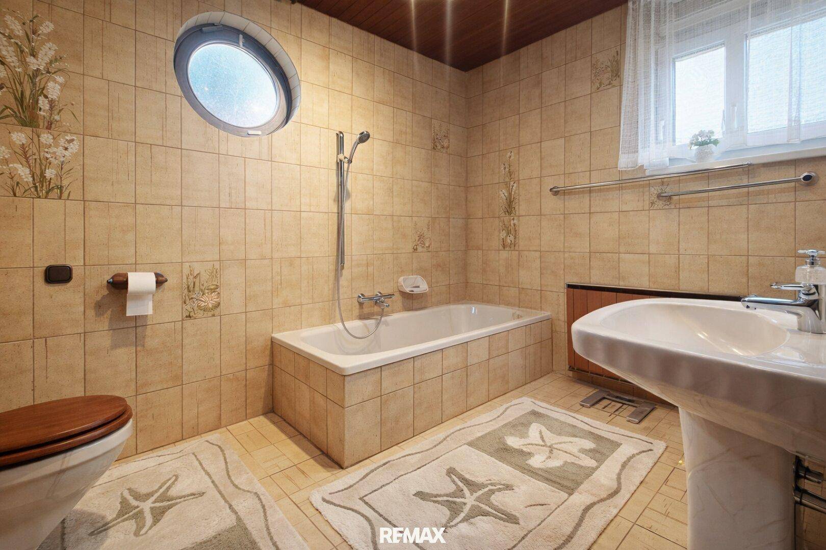 Gefliestes Badezimmer mit Badewanne, Waschbecken und einem runden Fenster.