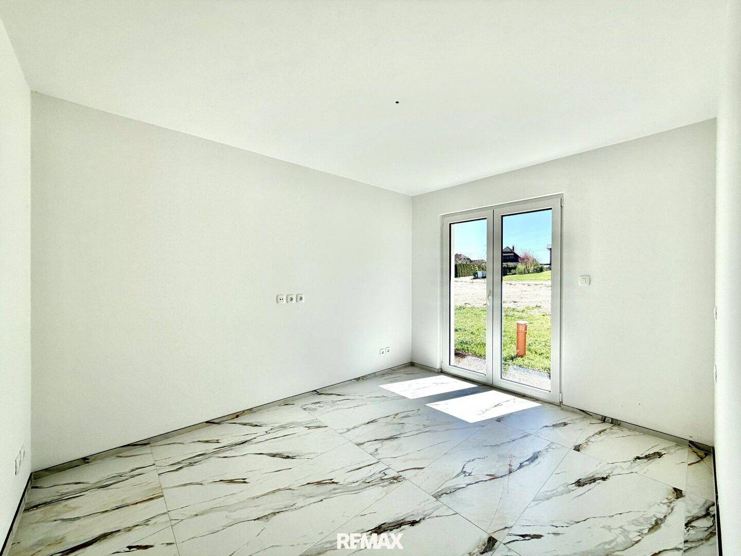 Leerer Raum mit Zugang nach draußen durch eine Glastür und modernen Marmorfliesen.