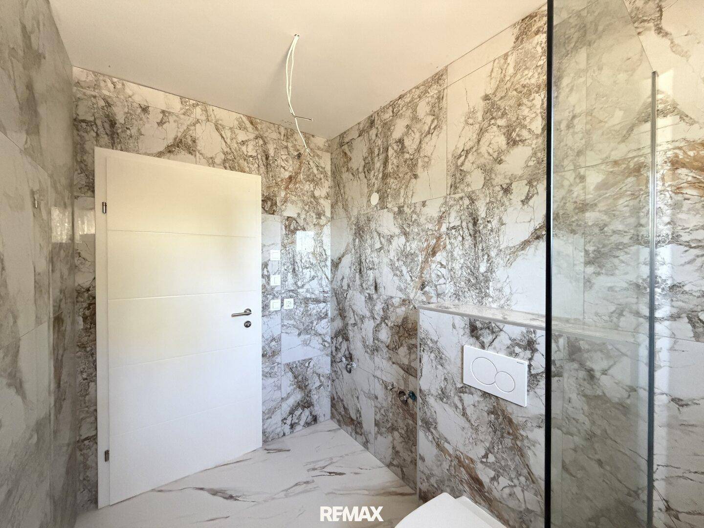 Modernes Badezimmer mit eleganten Marmorfliesen an Wänden und Boden, inklusive Duschbereich.