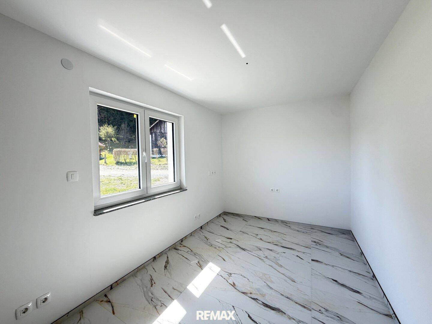 Leerer Raum mit einem Fenster, das viel Tageslicht hereinlässt, und Marmorfliesenboden.