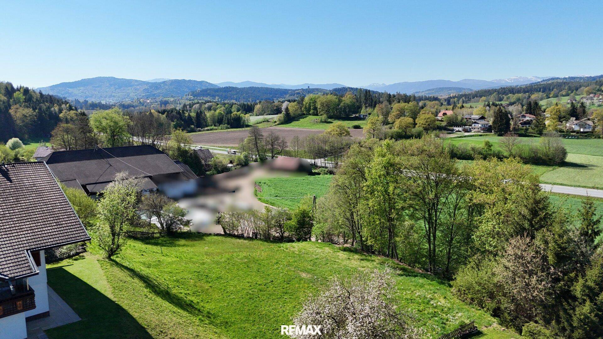 Weitläufige Luftaufnahme einer ländlichen Gegend mit Feldern, Häusern und Bergen am Horizont.
