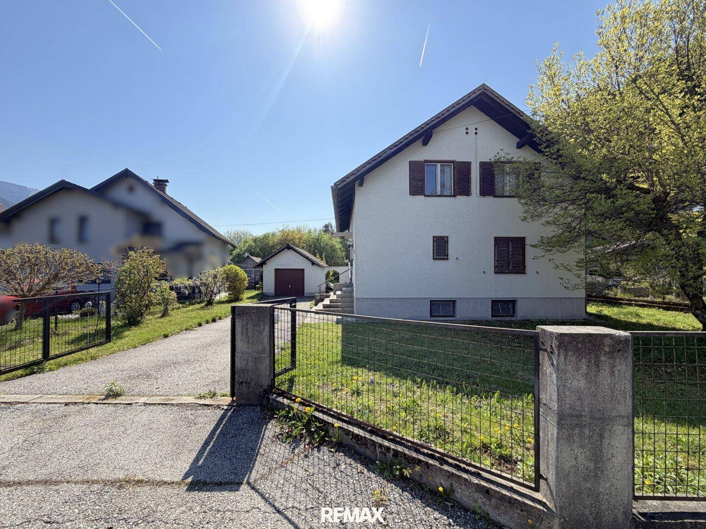 Vorderansicht des Hauses mit Einfahrt, Zaun und Garage im Hintergrund.