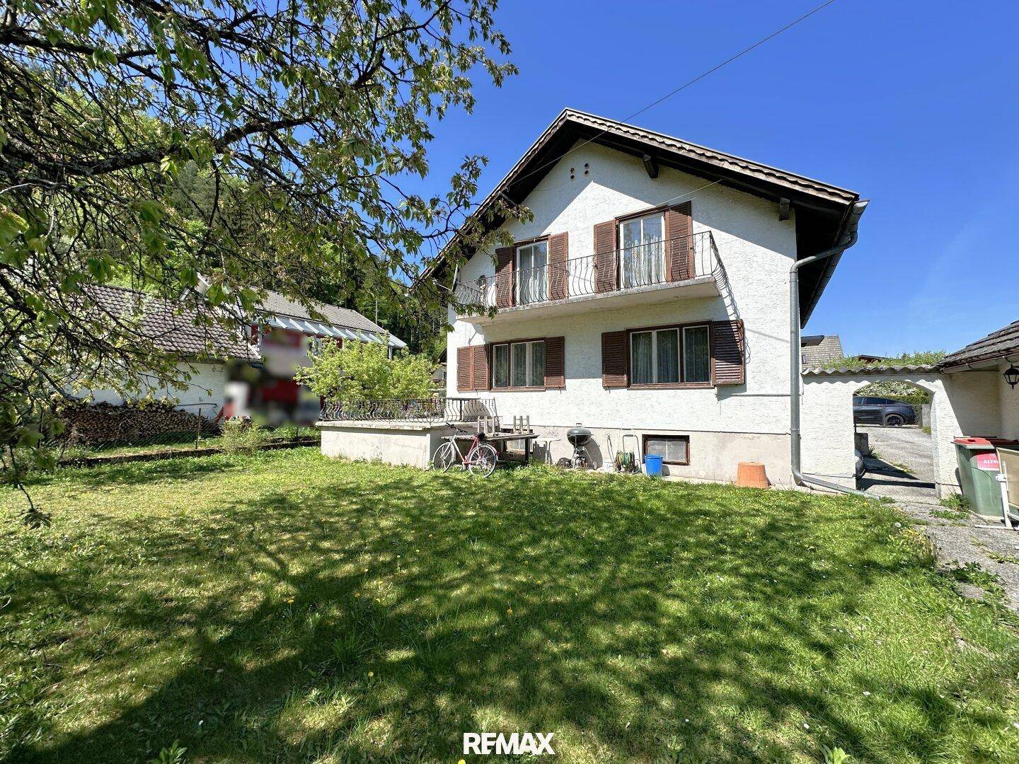 Hausansicht vom grünen Garten aus mit Balkon und kleiner Terrasse.