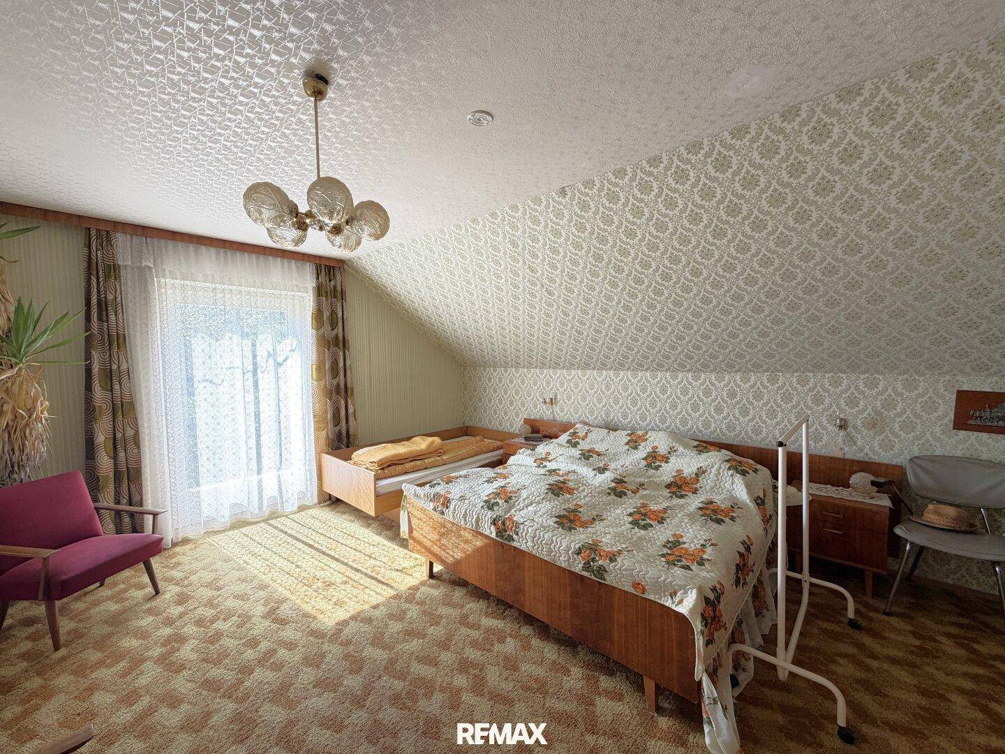Schlafzimmer im Dachgeschoss mit gemusterter Tapete, Teppichboden und schrägen Wänden.