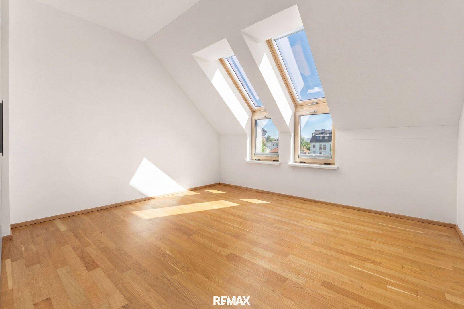 Helles Schlafzimmer mit Holzboden und schrägen Wänden, beleuchtet durch Dachfenster.