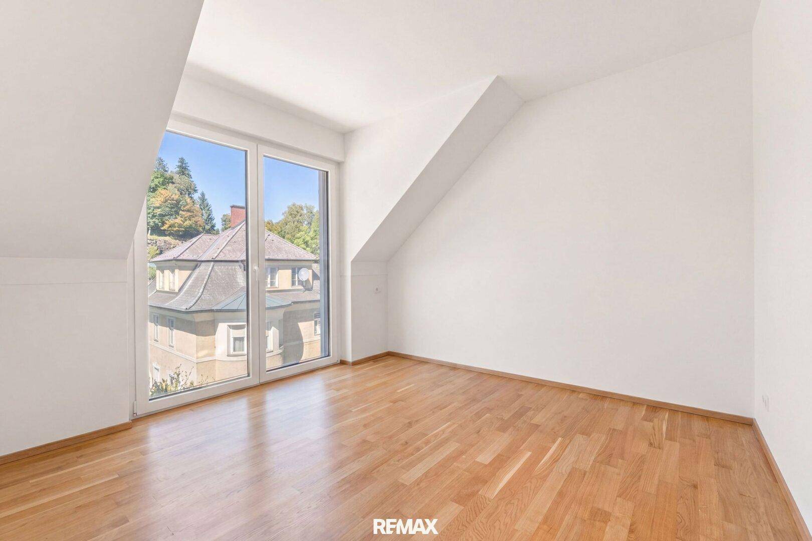Geräumiges Schlafzimmer mit Holzboden und großer Fensterfront, die viel Licht hereinlässt.