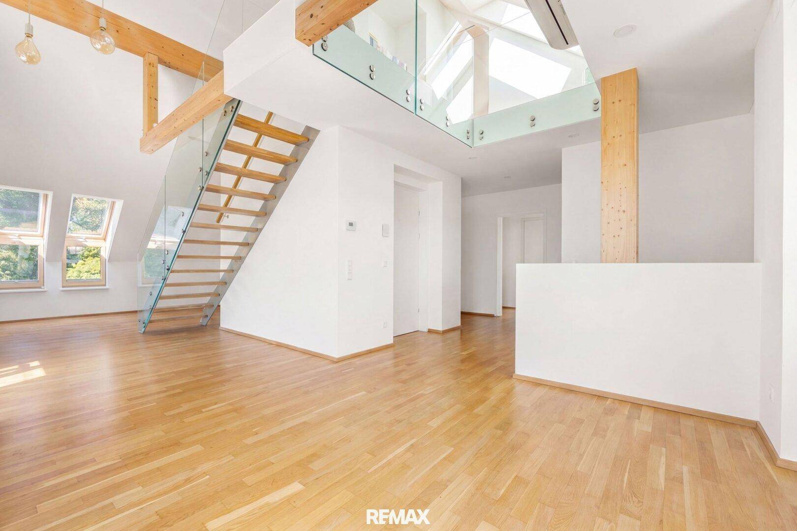 Geräumiger, heller Wohnbereich mit Holztreppe und Glasgeländer, offen gestaltet.