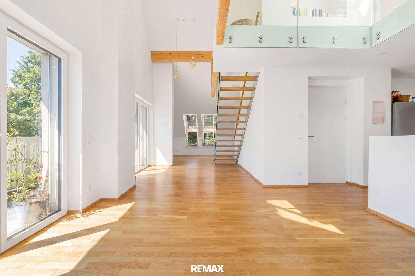 Lichtdurchfluteter Wohnbereich mit Holzboden, hohen Decken und Zugang zu einem Balkon.