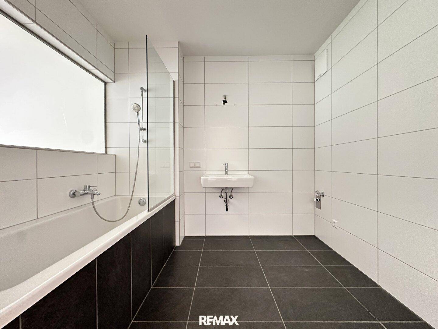 Modernes Badezimmer mit Badewanne, Dusche und dunklen Bodenfliesen.