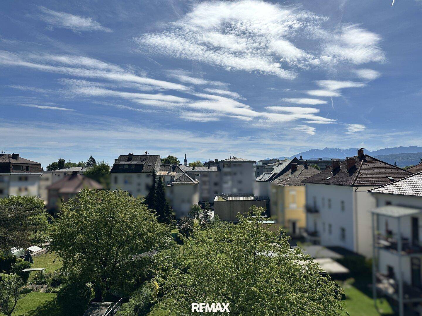 Panoramablick über die Stadt mit Wohngebäuden, viel Grün und Bergen im Hintergrund.
