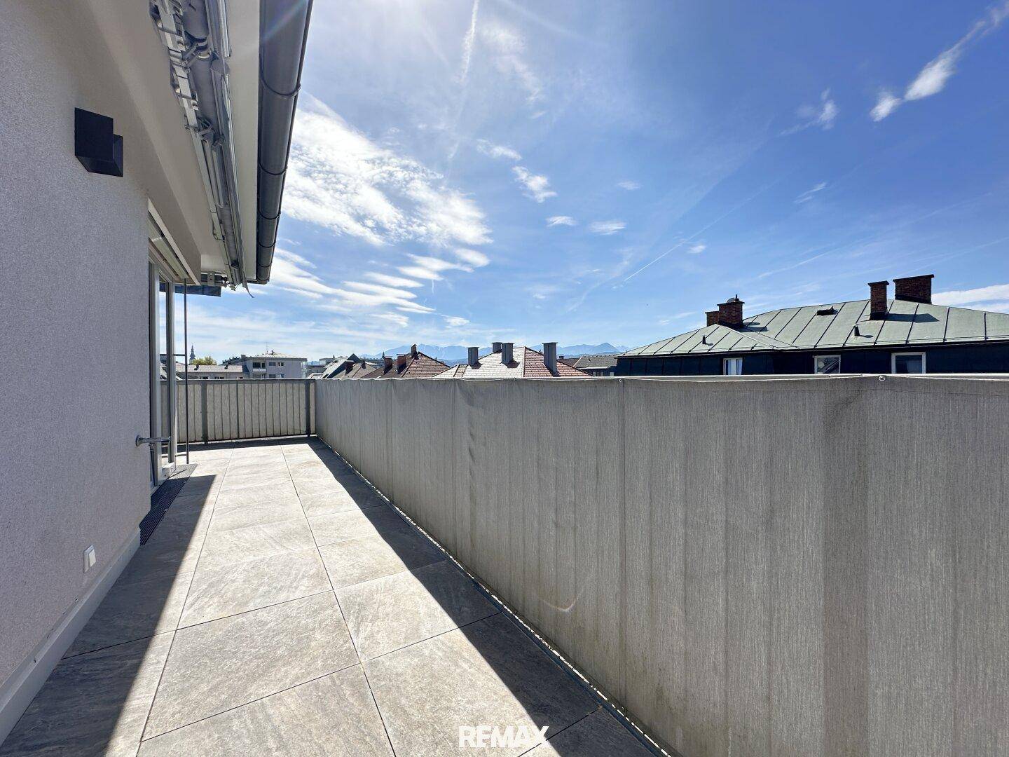 Lange, geflieste Terrasse mit Sichtschutz und sonnigem Ausblick auf die Umgebung.