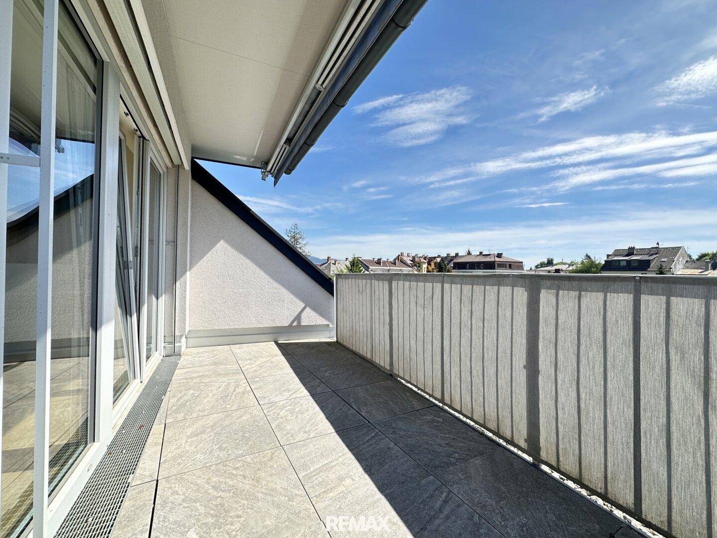 Geräumige Dachterrasse mit Fliesenboden und Blick auf die Umgebung unter blauem Himmel.