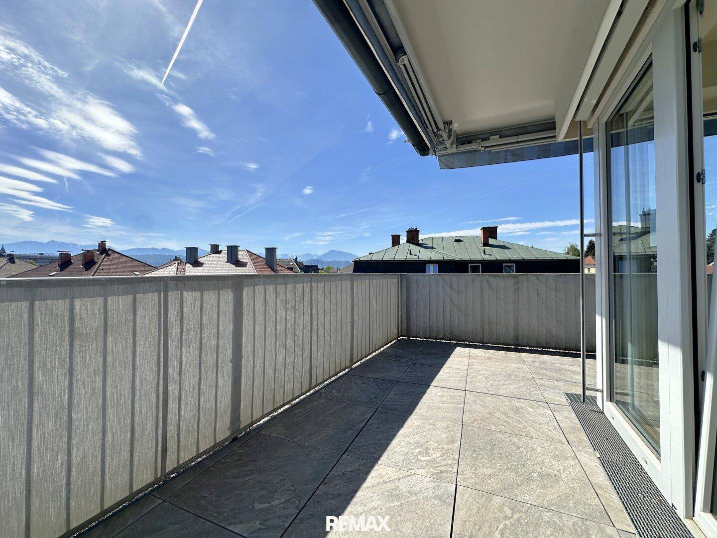 Sonniger Terrassenbereich mit Fliesenboden und weitem Blick über die Dächer der Stadt.