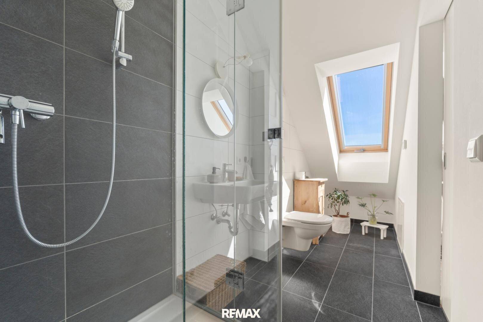 Helles Badezimmer mit Dusche, WC und Dachfenster, modern gefliest.