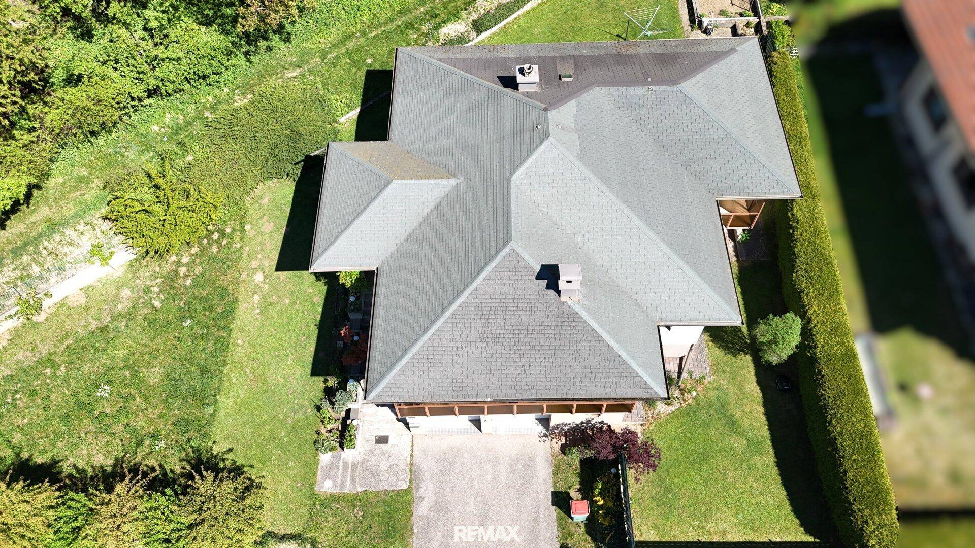 Dachansicht des Hauses mit mehreren Giebeln und umgebenden Grünflächen unter blauem Himmel.