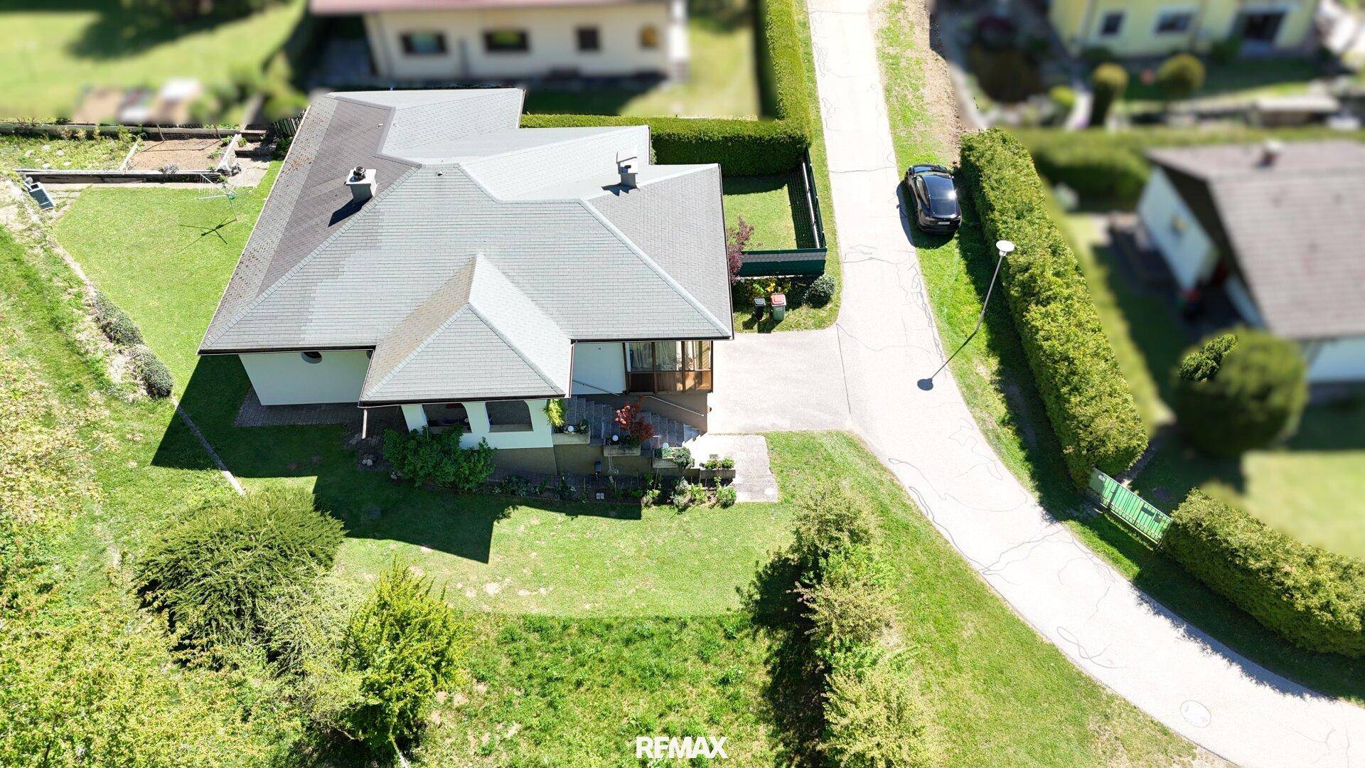 Luftaufnahme des Hauses mit Satteldach, umgeben von einem grünen Garten und einer Zufahrt.