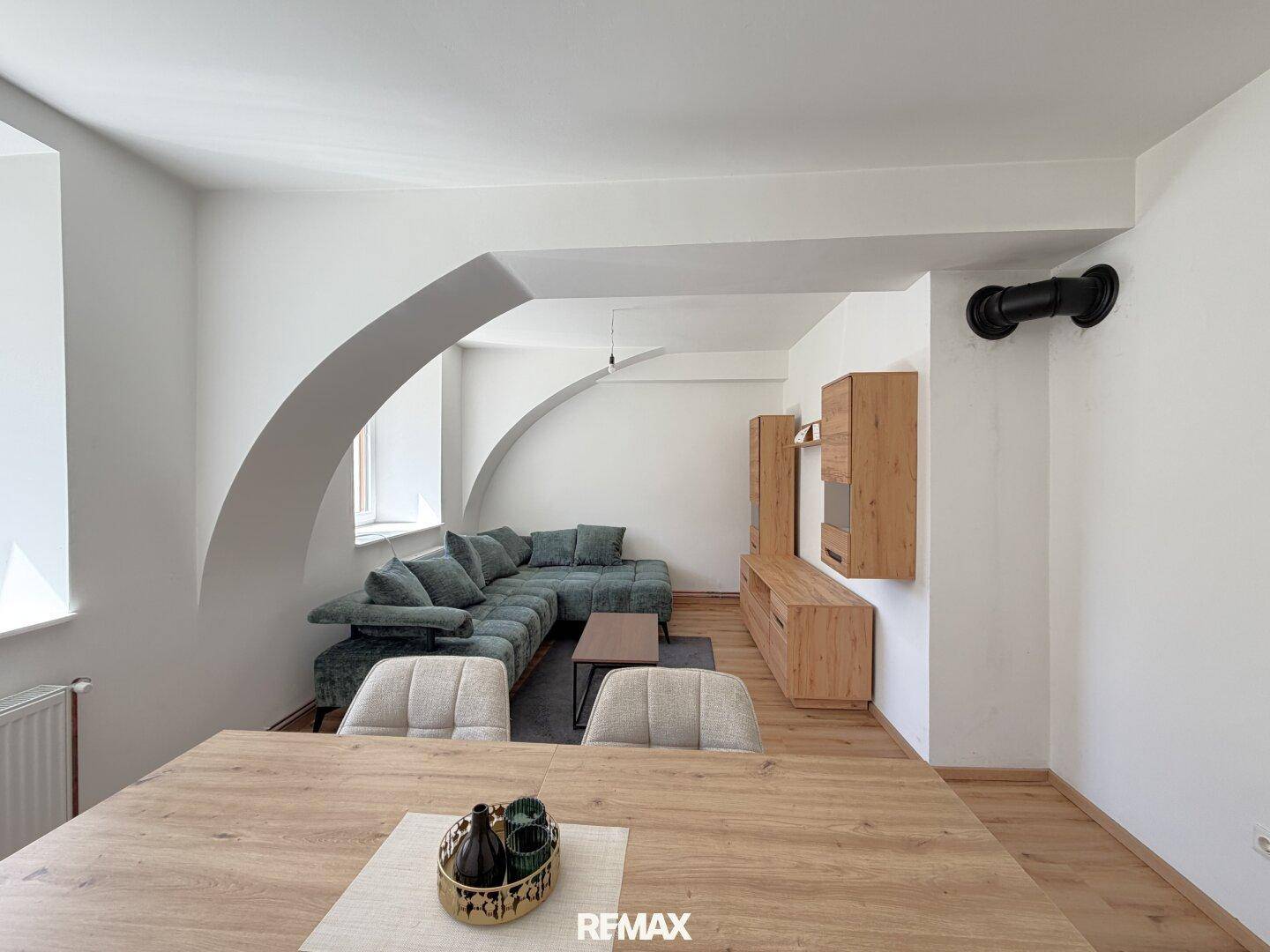 Heller Wohn- und Essbereich mit Holzboden, Esstisch und gemütlicher Sofaecke unter Dachschrägen.