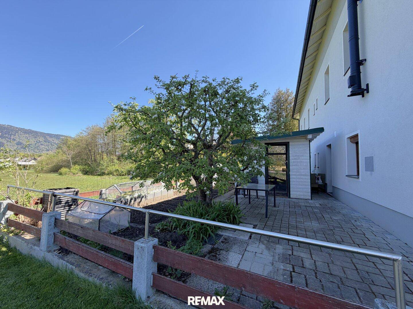 Seitlicher Blick auf das Haus mit gepflasterter Terrasse, Obstbaum und weitem Blick ins Grüne.