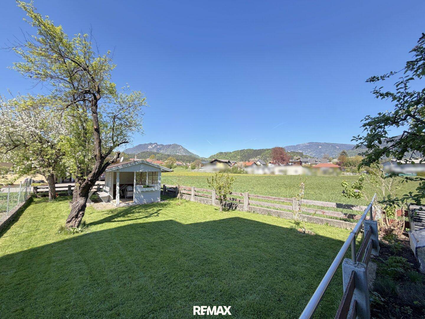 Weitläufiger Rasenbereich mit Gartenhaus und Panoramablick auf die umliegende Berglandschaft.