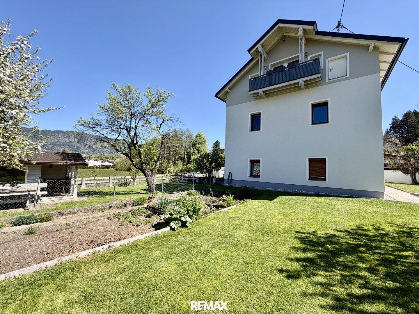 Hausfassade mit gepflegtem Gartenbereich, Gemüsebett und Blick auf die umliegende Landschaft und Berge.