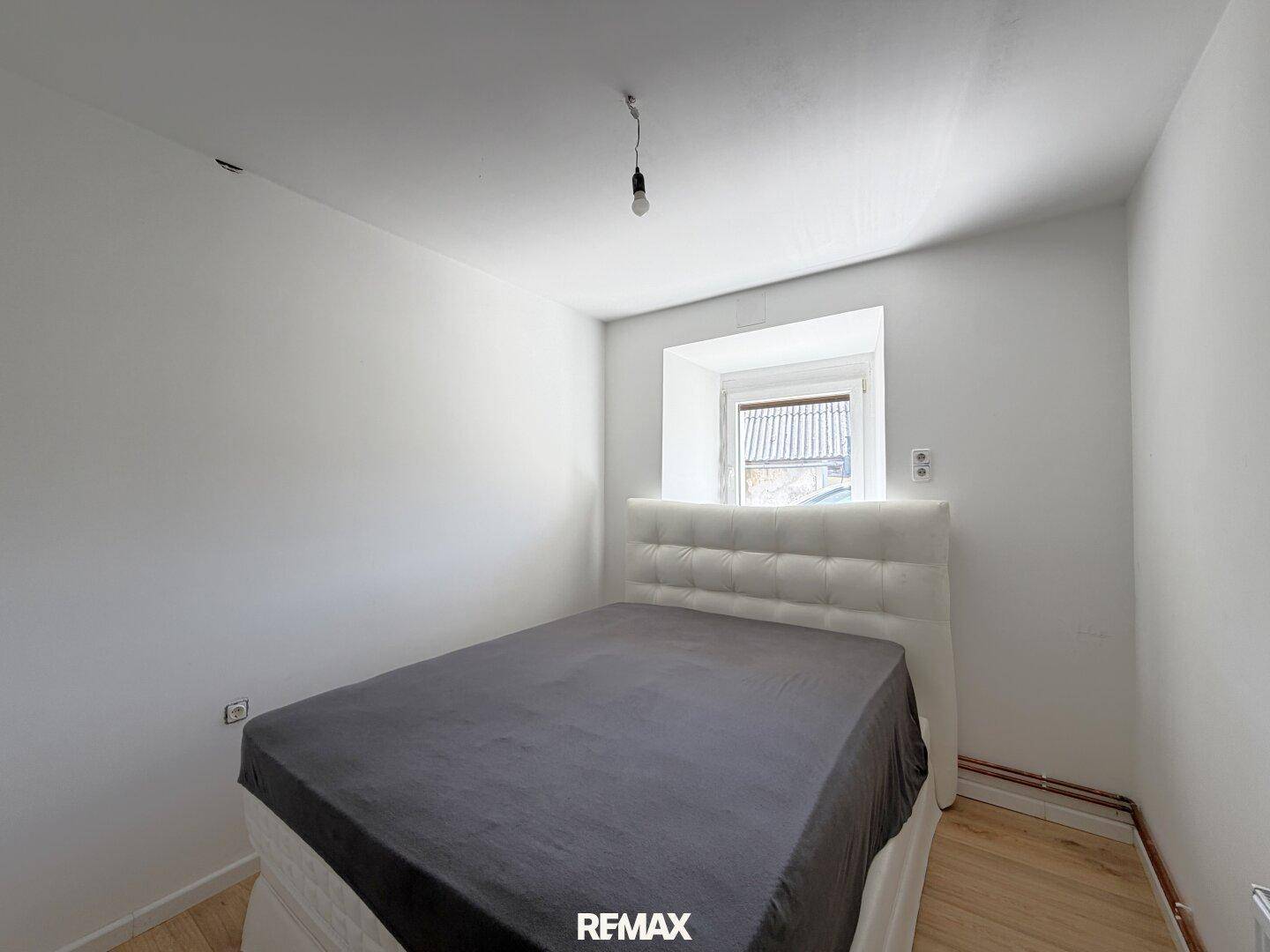 Schlichtes Schlafzimmer mit Doppelbett, Holzboden und einem Fenster für natürliches Licht.