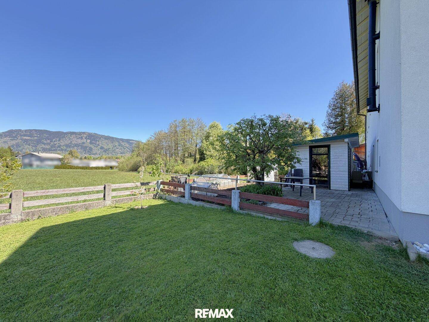 Großer Rasenbereich mit Holzzaun, angrenzender Terrasse und weitem Blick auf die grüne Landschaft.