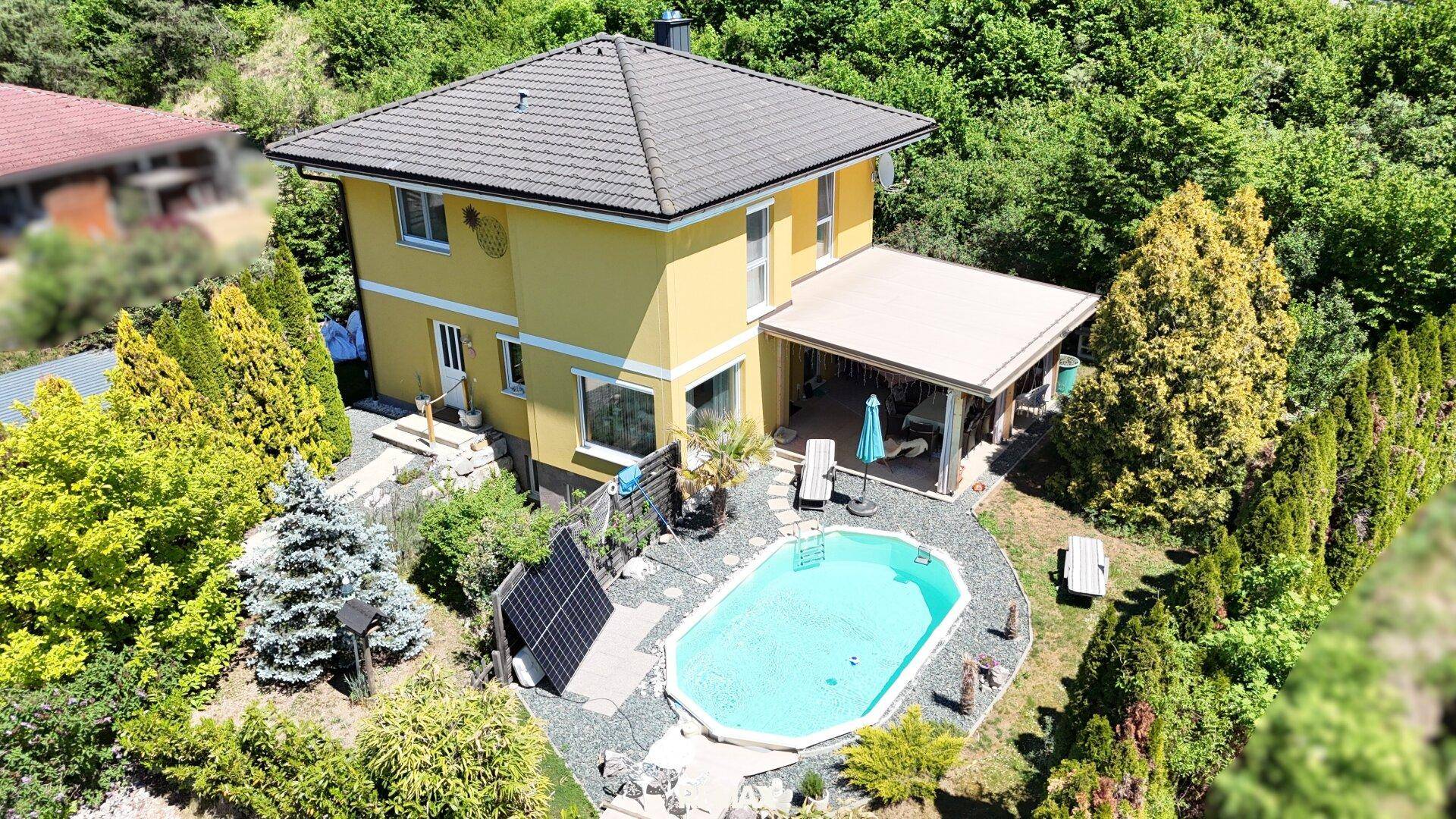 Nahaufnahme des gelben Hauses mit Pool, überdachter Terrasse und Photovoltaikanlage im Garten.