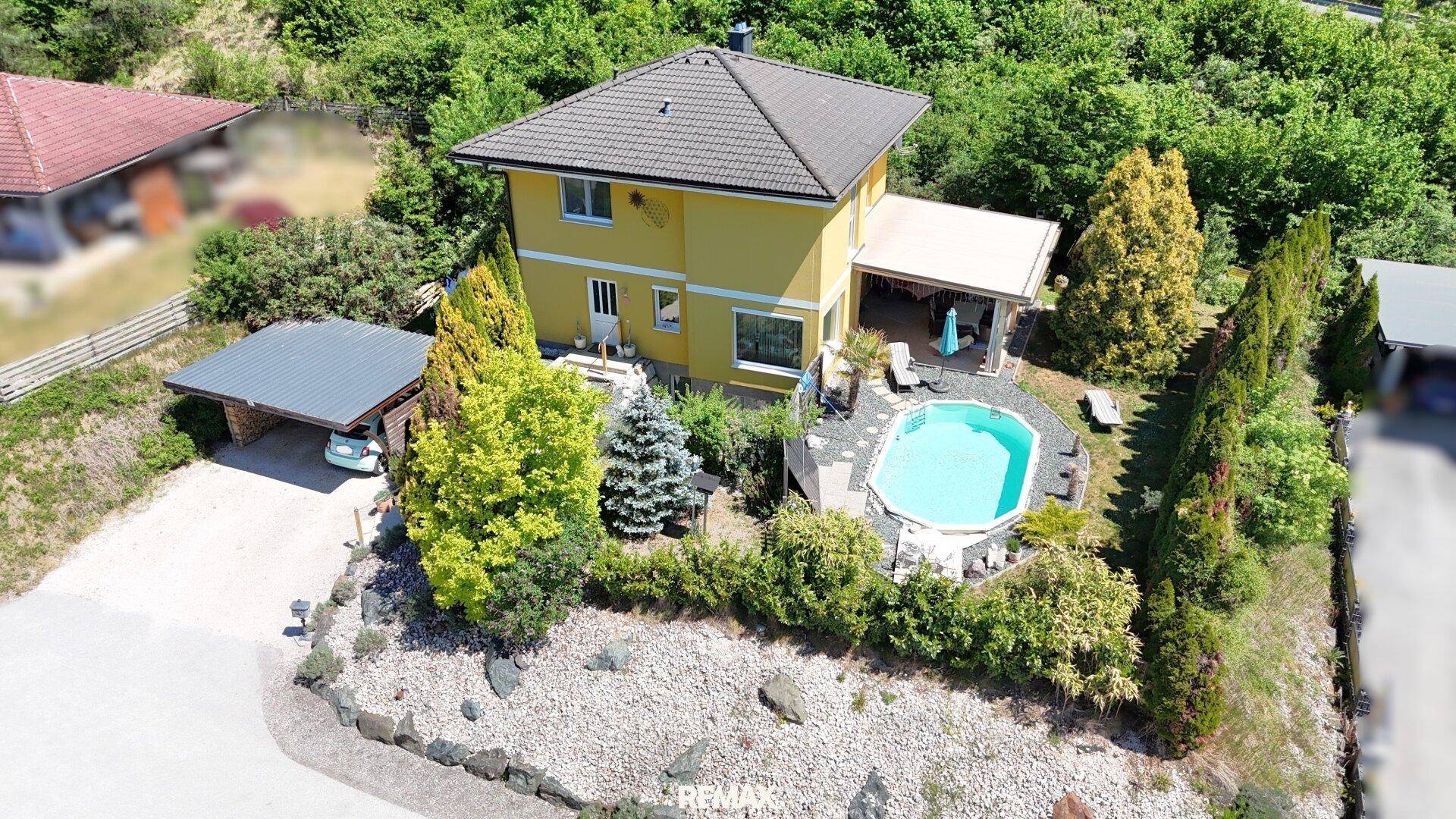 Übersicht des Anwesens mit gelbem Haus, Poolbereich und Carport, eingebettet in grüne Hügellandschaft.