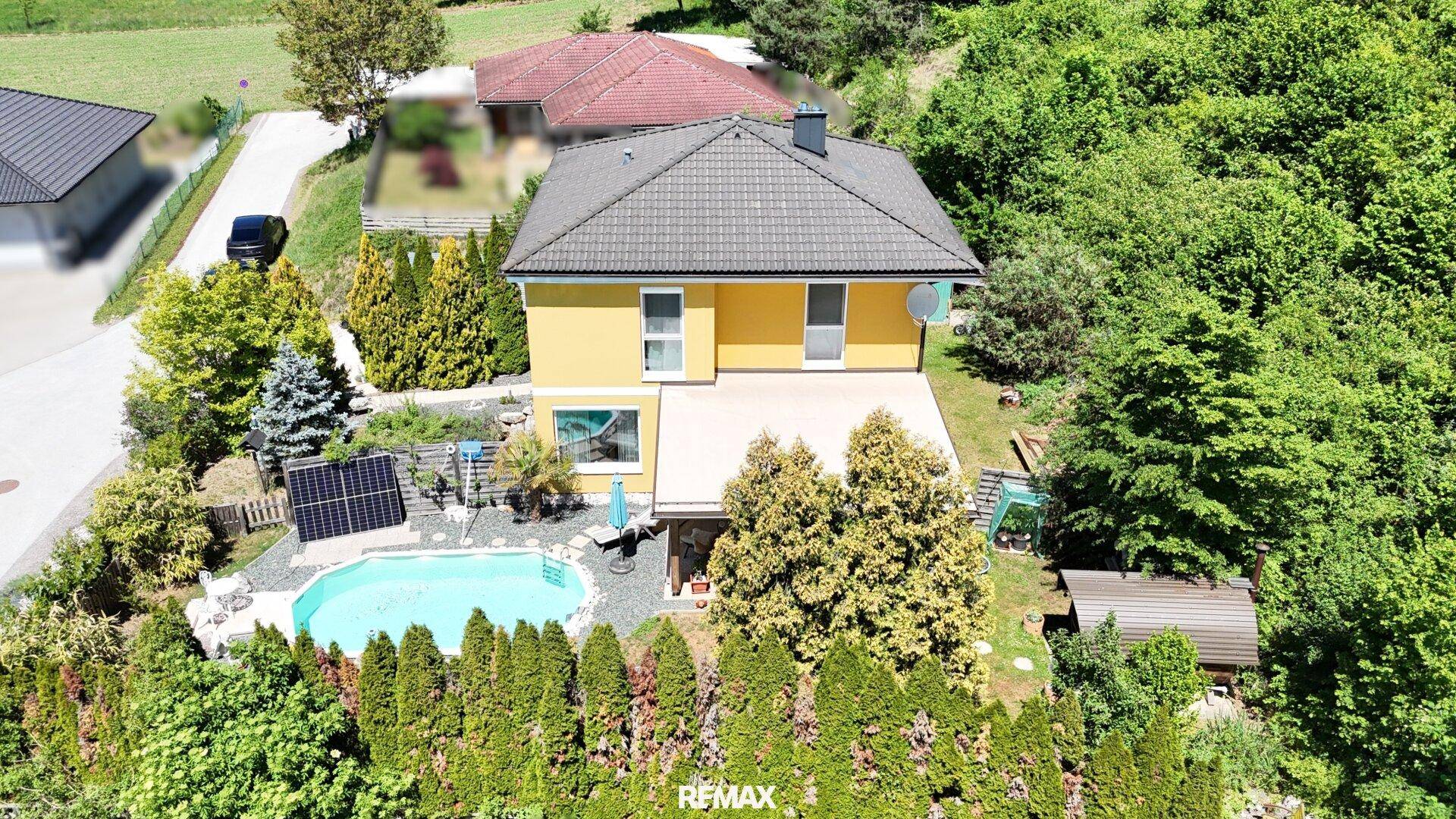 Ansicht des gelben Hauses von hinten mit Pool, Solaranlage und Gartenbereich unter blauem Himmel.