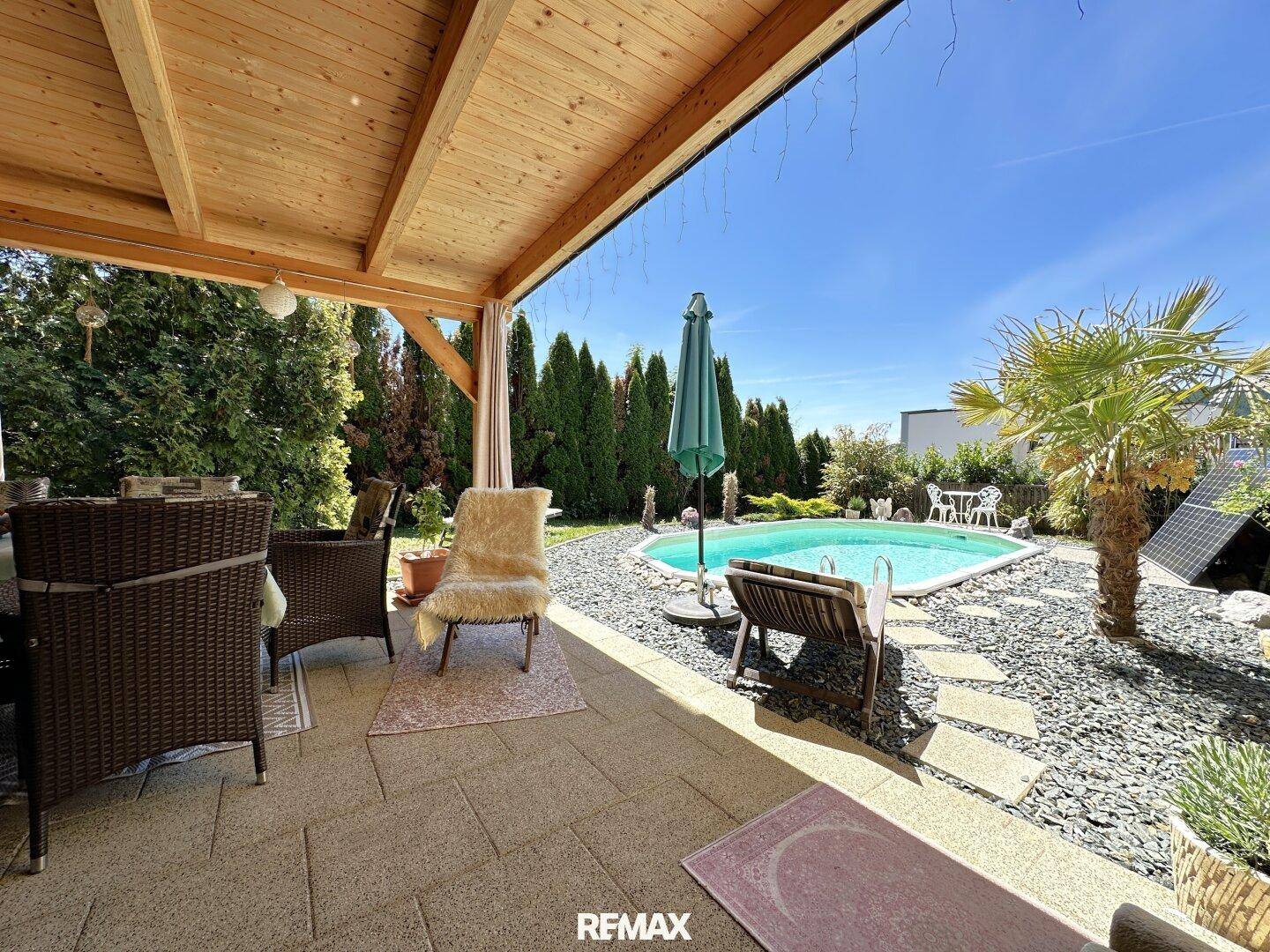Überdachte Terrasse mit Essbereich und Blick auf den Pool und den grünen Garten.