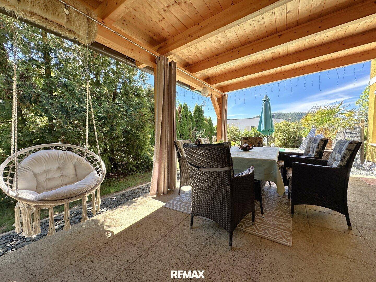 Geräumige überdachte Terrasse mit gemütlichem Essbereich und Hängesessel, ideal zum Entspannen.