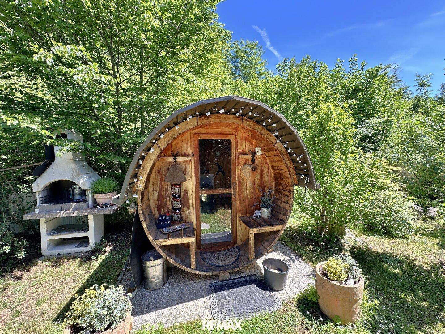 Fasssauna und gemauerter Grillplatz im grünen Garten, perfekt für Wellness und Unterhaltung.