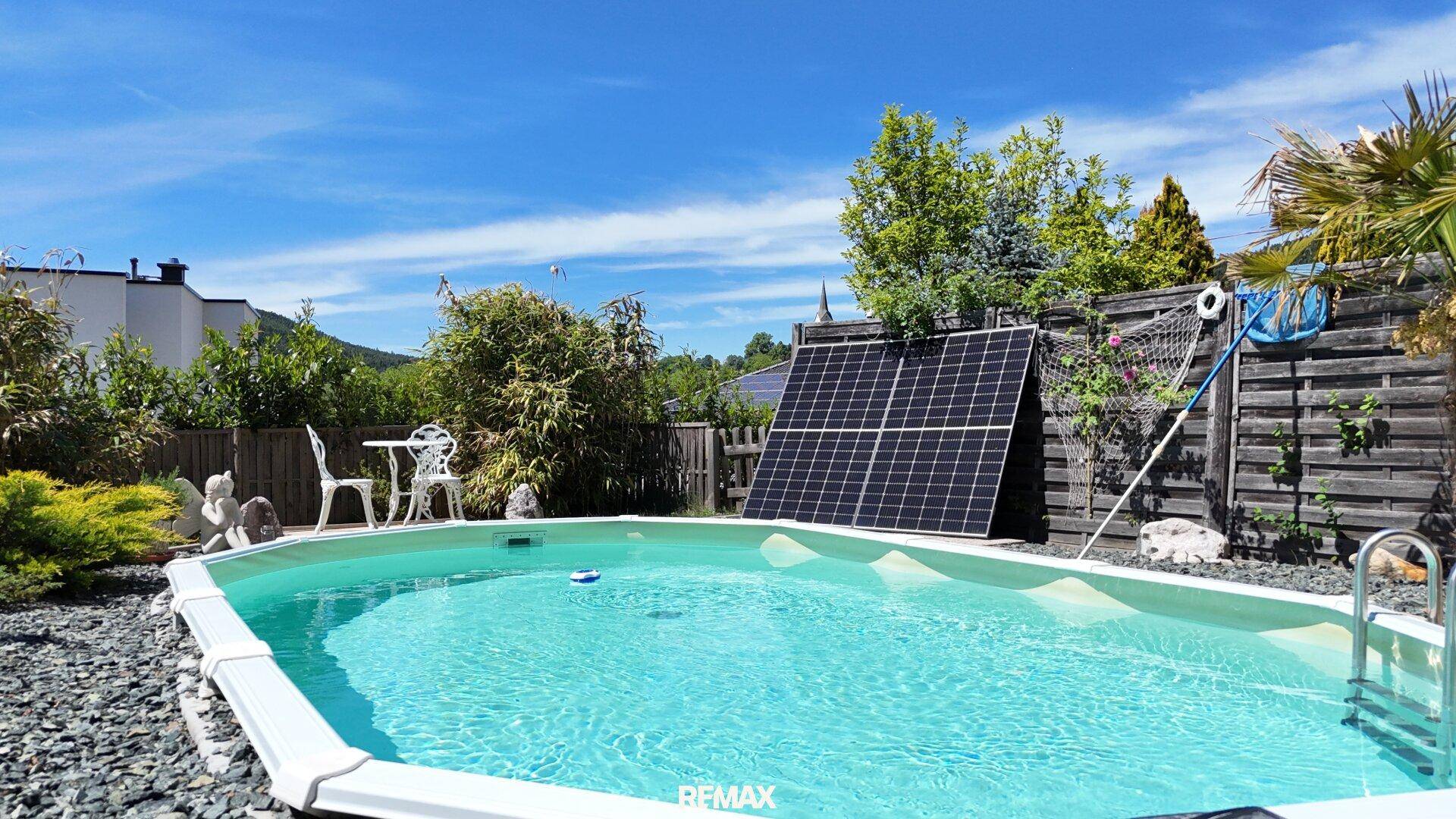 Außenpool mit Solarpaneelen und Gartenmöbeln, umgeben von einem Holzzaun.