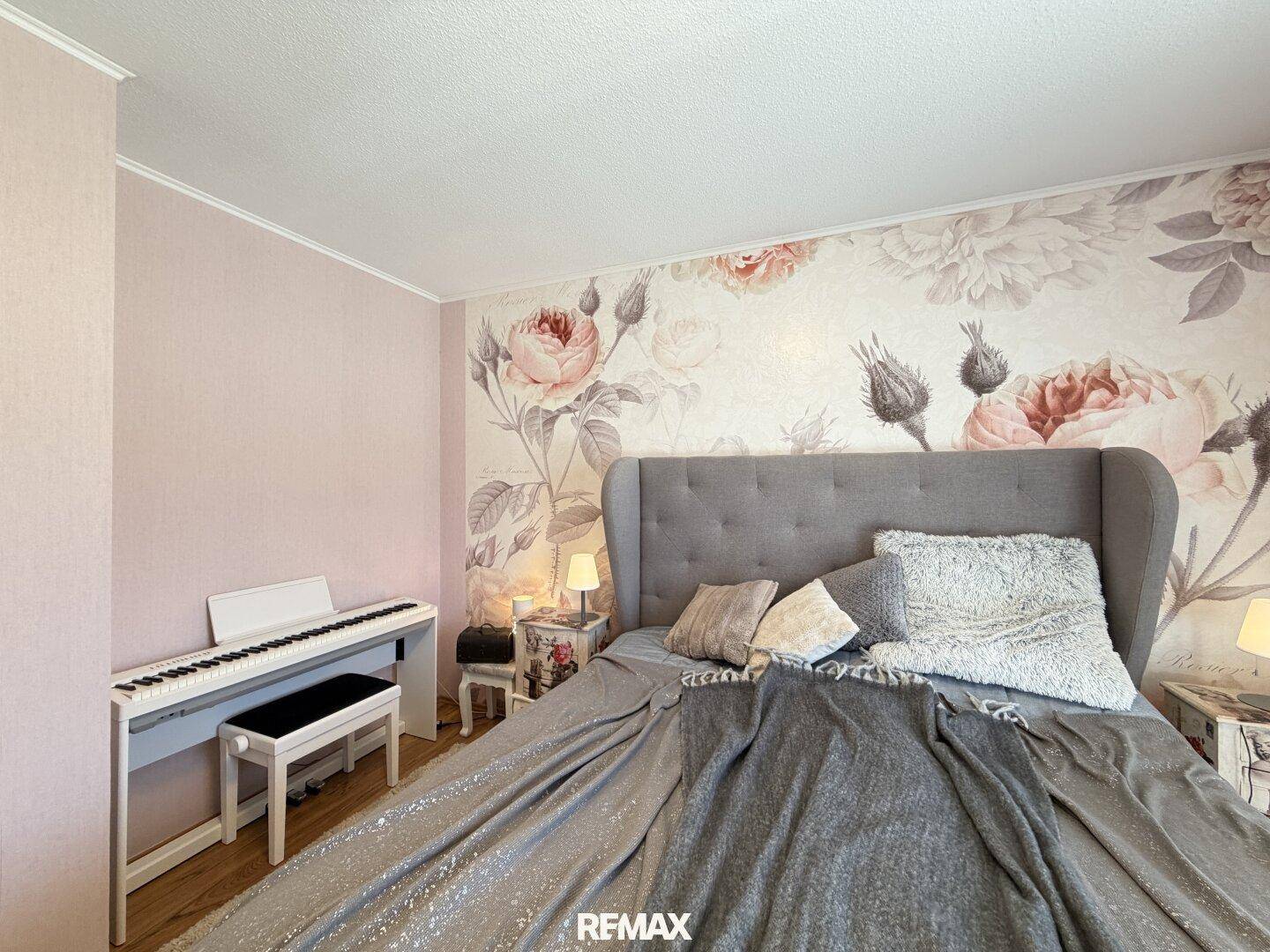 Schlafzimmer mit floraler Tapete, großem Bett und Klavier, schafft eine ruhige Atmosphäre.