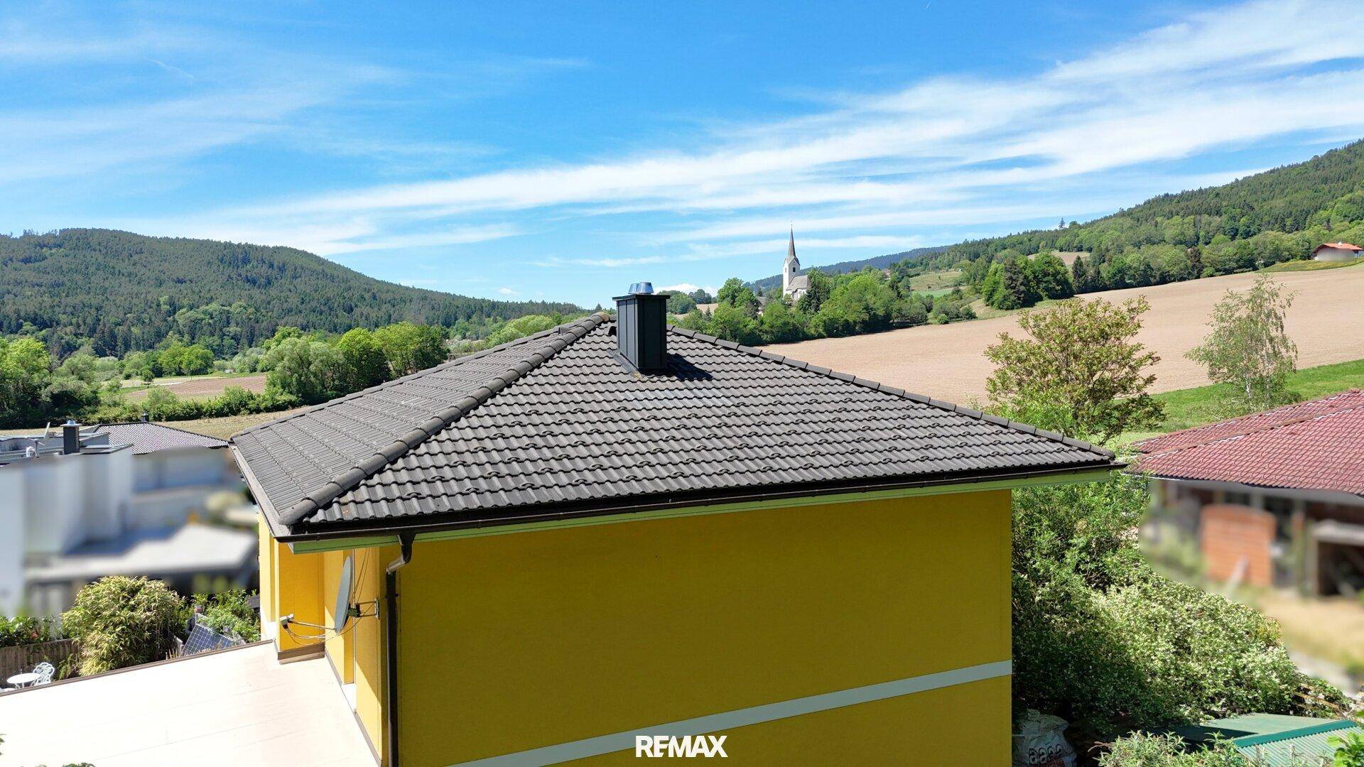 Dachansicht des Hauses mit Blick auf die weite Landschaft und eine Kirche in der Ferne.