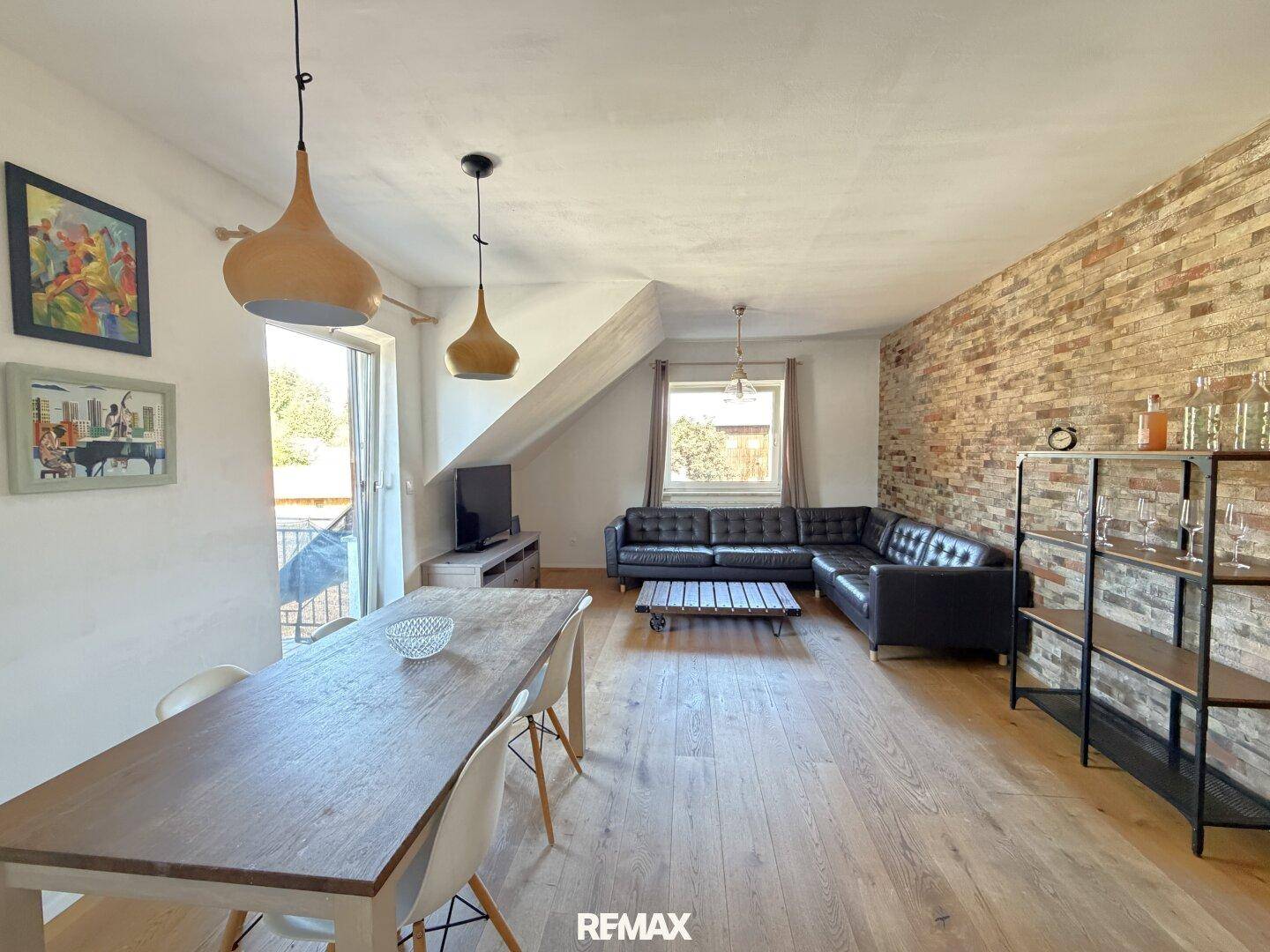 Geräumiger Wohn-Essbereich mit Holzboden, Ziegelwand und Zugang zu einem Balkon.