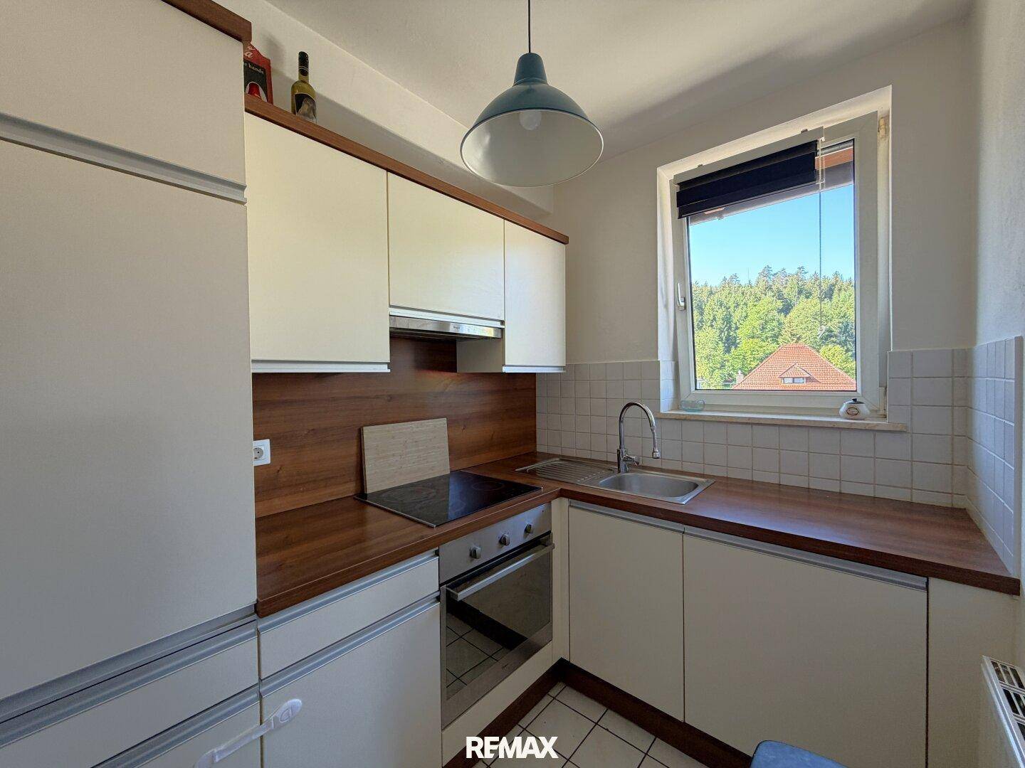 Funktionale Küche mit weißen Schränken, Holzarbeitsplatte und Fenster mit Blick ins Grüne.